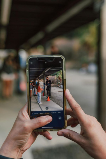 An iphone is held up and shows a scene of a child talking to an older person. The suggestion is that a photo is being taken on the phone.