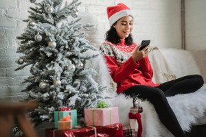 A person sitting next to a Christmas tree, checking their phone and smiling.